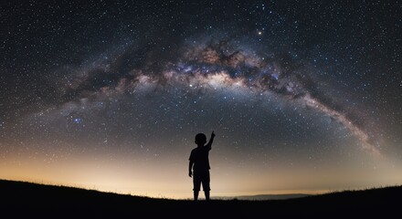 Fototapeta premium A lone child gazes upwards at the magnificent arc of the Milky Way galaxy stretching across the vast expanse of the night sky above a silhouetted landscape