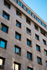 A multi-story building showcases urban architecture. Its facade features numerous windows and air conditioning units, reflecting the practicality of city life among the buildings under a bright sky.