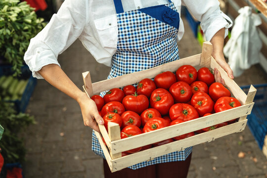 Cheerful small business owner posing at farmers market, wearing apron looking at camera. Female food marketplace vendor selling fresh organic produce and standing at local market. - Powered by Adobe