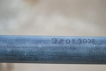 The date "27.05.2025" is etched into a horizontal metal surface, captured in natural light with a softly blurred background.