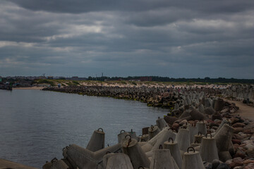 Concrete tetrapods line the shore forming a breakwater, with a calm sea and overcast sky in an...
