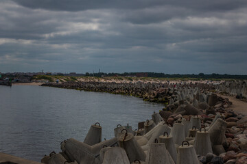 Concrete tetrapods line the shore forming a breakwater, with a calm sea and overcast sky in an...