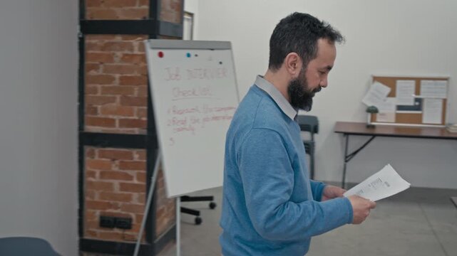 Medium panning shot of Caucasian male teacher giving resume samples to group of multiracial prison convicts serving criminal sentences in penitentiary institution, while conducting adaptation course