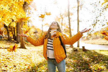A happy woman stands in an autumn park and cheerfully throws colorful leaves up. A young woman in a...