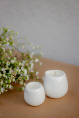 Minimalistic white ceramic candles and small white flowers on a brown background. Cozy and calm atmosphere, natural light, soft focus. Home decor and aromatherapy concept.