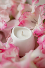 White ceramic candles on a soft surface with blurred pink flowers in the background. Minimalist spa composition for relaxation, wellness, aromatherapy, and home decor concepts.
