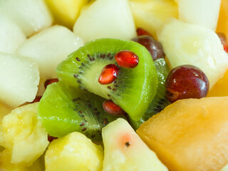 A fruit bowl with kiwi, grapes, melon, pineapple, and pomegranates
