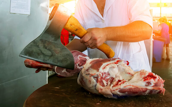 Skilled butcher using cleaver to chop large piece of meat in bustling market environment during daylight hours - Powered by Adobe
