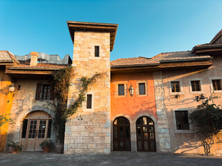 Charming rustic building with stone tower and colorful facade surrounded by greenery under clear blue sky, old town European streets with stone houses