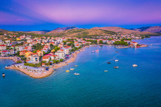 Drone photo of Zaboric at dusk showing glowing village lights, calm Adriatic shoreline, houses by the sea and a peaceful Mediterranean atmosphere under the fading evening sky