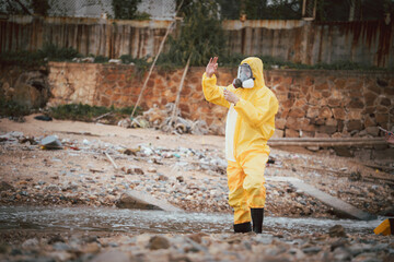 Water quality inspection, Environment scientist in hazmat suit holding a water sample vial in a polluted industrial area. Concept of environmental analysis, factory wastewater, and hazard assessment