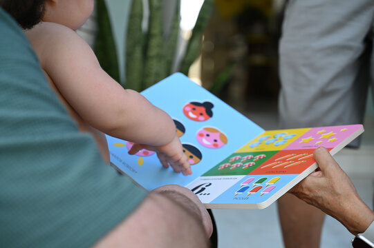 toddler pointing at pictures in baby book, early childhood learning through play, family interaction with educational board book, baby interacting with book


