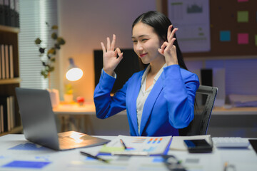 Asian businesswoman showing ok sign while working late at night in office