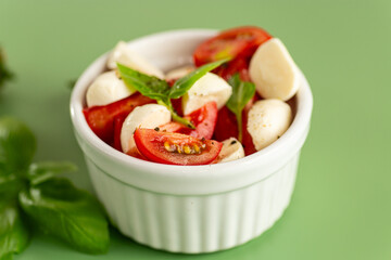 italian caprese salad in a white ceramic bowl on a green background