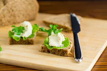 Slice of rye bread with cheese spread and greens on the table