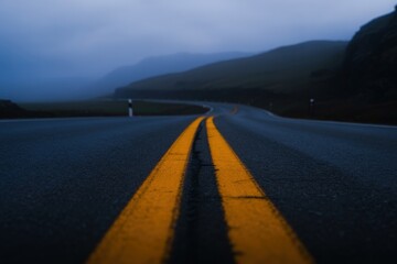 Fototapeta premium A foggy road stretches into the distance, winding through a mountainous landscape