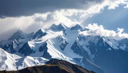Obraz premium Majestic Snow-Capped Mountains Under Dramatic Clouds with Sunlight Breaking Through the Sky