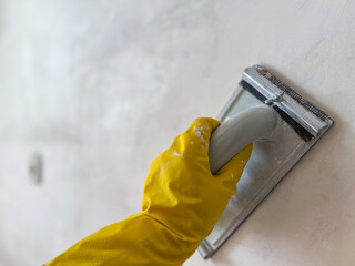 Construction worker sanding wall with sandpaper holder and wearing yellow gloves