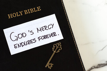 God's mercy endures forever handwritten quote with holy bible book and ancient key. Top view. Christian biblical concept.