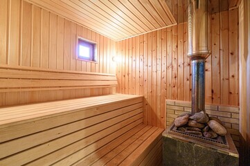 cozy sauna with wooden benches, walls, and ceiling. There's a stone-filled stove and a small window letting in light