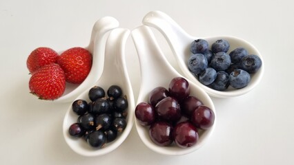 Four white, curved ceramic bowls each contain different berries: strawberries, blackcurrants, cherries , and blueberries. Mixed berries in white fruit bowls. Healthy eating concept. 