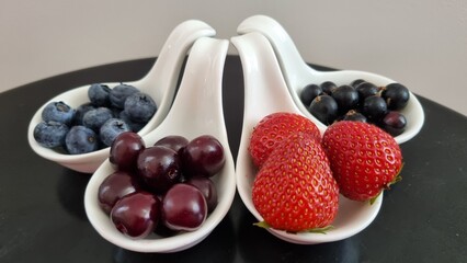 Four white, curved ceramic bowls each contain different berries: strawberries, blackcurrants, cherries , and blueberries. Mixed berries in white fruit bowls. Healthy eating concept.