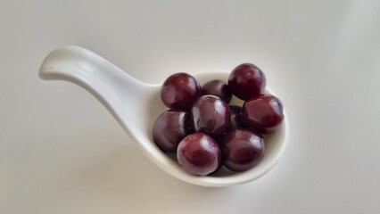 red cherries in a bowl, white curved ceramic fruit bowl, contains cherries, Healthy eating concept. Top view.A white curved ceramic bowl contains several dark red cherries.
