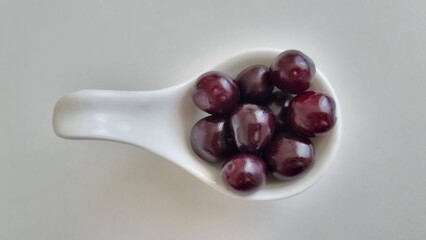 white curved ceramic fruit bowl, contains cherries, Healthy eating concept. Top view. A white curved ceramic bowl contains several dark red cherries.