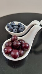 White curved ceramic fruit vase containing red cherries, blueberries on the black table. Mixed berries in white fruit bowls. Healthy eating concept. Macro 
