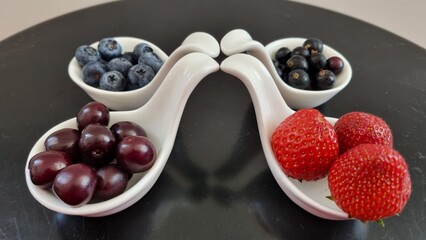 Four white, curved ceramic bowls each contain different berries: strawberries, blackcurrants, cherries , and blueberries. Mixed berries in white fruit bowls. Healthy eating concept.