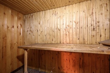 room clad in wooden planks, including the ceiling, with a sturdy wooden counter or shelf in the...