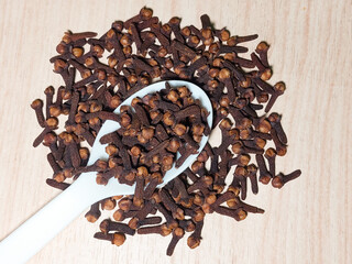 Dried clove spice in a white spoon on the table. Aromatic dried clove flower buds. Dried clove spice.
