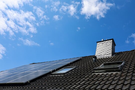 Photovoltaic panels providing green energy on a rooftop with chimney and skylights