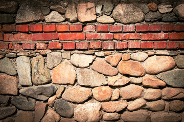 Stones and bricks form a textured wall in a rustic setting with natural lighting