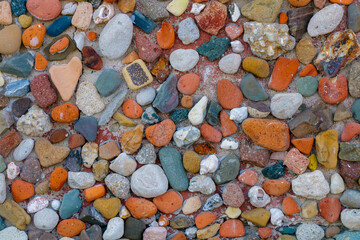Colorful collection of smooth stones and pebbles displayed on a natural surface in a sunny outdoor setting with textures and patterns highlighting the variety of shapes and hues