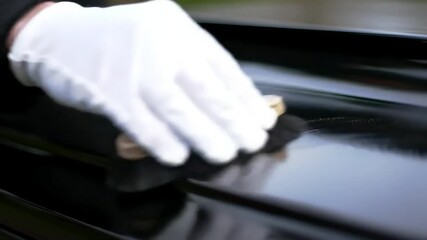 A skilled hand meticulously cleans the polished surface of a black piano, showcasing elegance and craftsmanship.