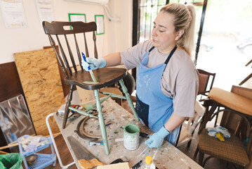 Young woman artisan refurbishing old furniture in small workshop