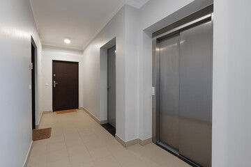 Interior of a modern apartment building hallway with a stainless steel elevator and entrance doors. This empty common corridor in a new residential complex is a perfect real estate background.