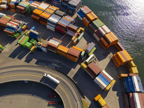 Aerial view of a vibrant array of stacked shipping containers at the port, contrasting with the dark water and the curving road below, Oslo, Norway.