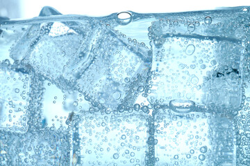 Soda water with bubbles and ice cubes in glass, closeup