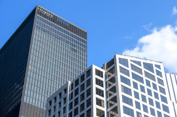 Obraz premium The black tower rises behind a white office building with slanted window panels under a bright blue sky., Toronto, Canada
