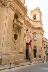 Historic sandstone church facade with Maltese flags in Valletta, Malta.