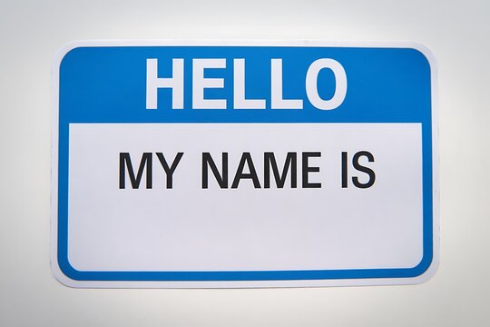 A blank blue and white name tag sticker with the words hello my name is printed in bold white letters on a light gray background