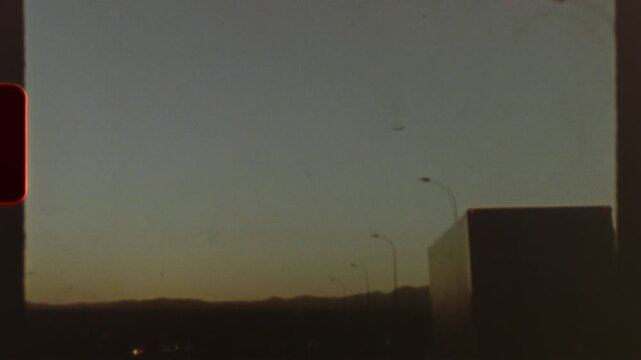 Filmed on super 8 film Grainy vintage 8mm footage, capturing highway stretching across twilight landscape with approaching road signs and distant plane silhouetted against dusky evening sky
