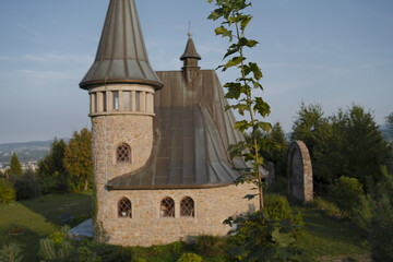 Naklejka premium a stone church with a tall steeple and a clock on it. The church has a sloped roof and is situated on a grassy hill.
