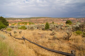 Rustic wooden fence winding through dry desert grassland with sagebrush and scattered juniper...