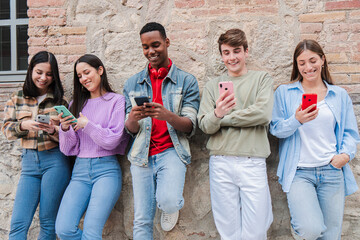 A lively group of five teenagers engaged with their smartphones, sharing moments and enjoying...