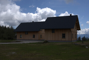 Obraz premium Modern wooden house nestled in a serene mountain landscape under a cloudy sky in the afternoon