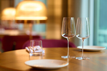 Elegant table with two empty wine glasses, plates, and napkins on a polished wooden surface in a cozy interior with warm lighting and inviting atmosphere