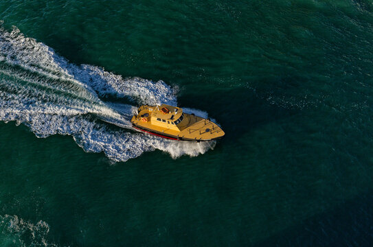 Pilot boat cruising at high speed on turquoise ocean water, aerial view